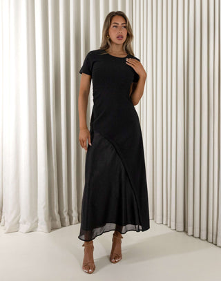 Woman wearing a black dress standing against a white curtain background Davina black contrast sheen maxi dress with short sleeves