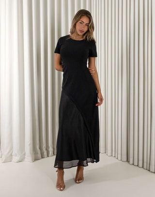 Woman wearing a black dress standing against a white curtain background Davina black contrast sheen maxi dress with short sleeves
