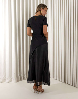 Woman wearing a black dress standing against a white curtain background Davina black contrast sheen maxi dress with short sleeves
