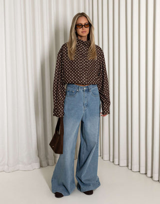 Person wearing a polka dot shirt and blue jeans against a white curtain background