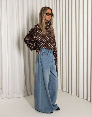 Person wearing a polka dot shirt and blue jeans against a white curtain background