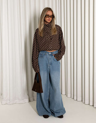 Person wearing a polka dot shirt and blue jeans against a white curtain background