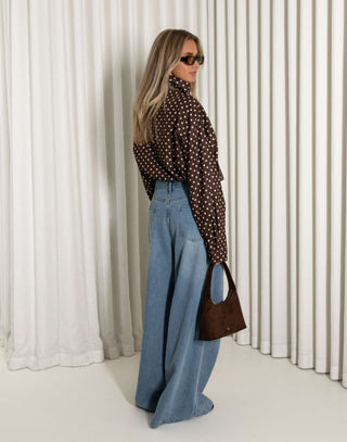 Person wearing a polka dot shirt and blue jeans against a white curtain background