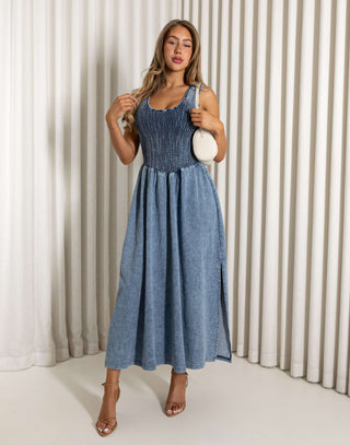 Woman wearing a blue dress holding a white handbag against a neutral background Eddie denim midi dress with shirred bust, racerback
