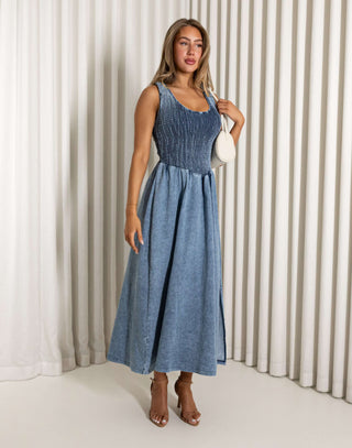 Woman wearing a blue dress standing against a white curtain background Eddie denim midi dress with shirred bust, racerback
