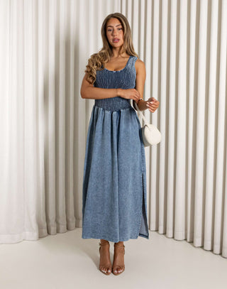 Woman wearing a blue dress standing against a white curtain background Eddie denim midi dress with shirred bust, racerback
