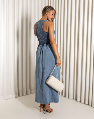 Woman wearing a blue dress holding a white clutch against a white curtain background Eddie denim midi dress with shirred bust, racerback
