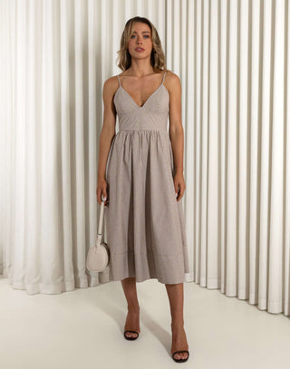 Woman wearing a beige dress standing against a white curtain background Emery brown fit and flare dress with flattering stripe placement