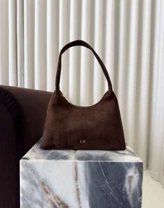 Brown handbag on a marble surface with a neutral background Erika brown faux suede shoulder bag