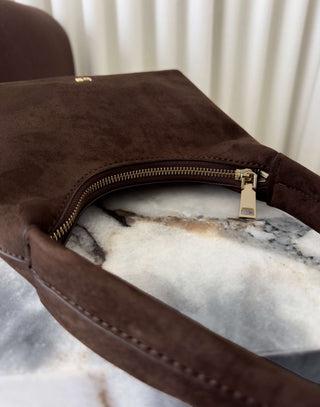 Brown leather clutch with gold zipper on a marble surface Erika brown faux suede shoulder bag