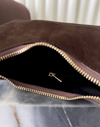 Brown leather clutch with gold zipper on a marble surface Erika brown faux suede shoulder bag