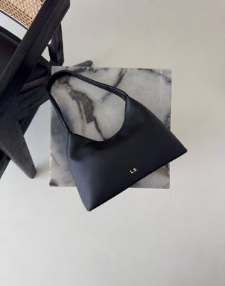 Black handbag on a marble block with a light gray background Erika black shoulder bag, compact, stand-flat base
