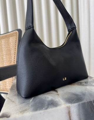 Black handbag with gold logo on a marble surface Erika black shoulder bag, compact, stand-flat base
