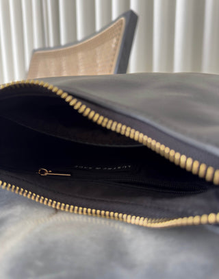 Close-up of a gray leather clutch with gold zipper on a marble surface. Erika black shoulder bag, compact, stand-flat base

