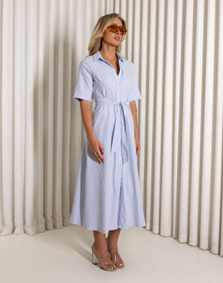 Woman wearing a blue and white striped dress with sunglasses against a neutral background Blue striped midi dress with collar and side pockets worn by model
