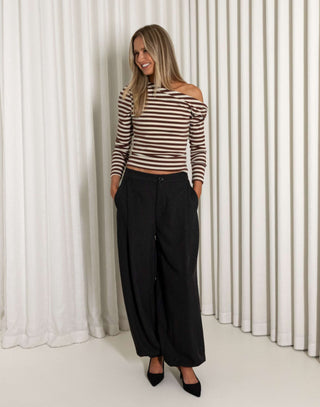 Woman wearing a striped top and black pants standing against a white curtain.
