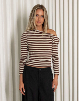 Woman wearing a striped top and black pants standing against a white curtain.