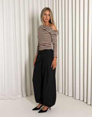 Woman wearing a striped top and black pants standing against a white curtain.
