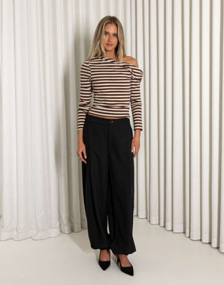 Woman wearing a striped top and black pants standing against a white curtain.