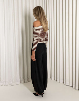 Woman wearing a striped top and black pants standing against a white curtain.