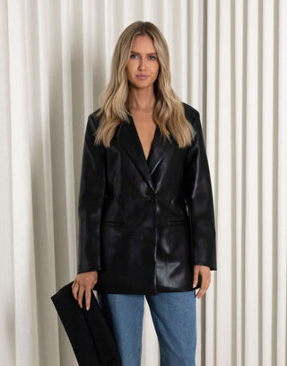 Woman wearing a black leather jacket and blue jeans against a white curtain background