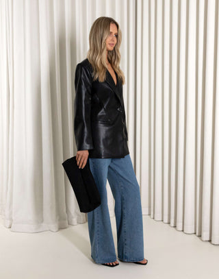 Woman wearing a black leather jacket and blue jeans against a white curtain background