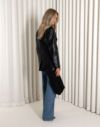 Person wearing a black leather jacket and blue jeans standing against a white curtain.