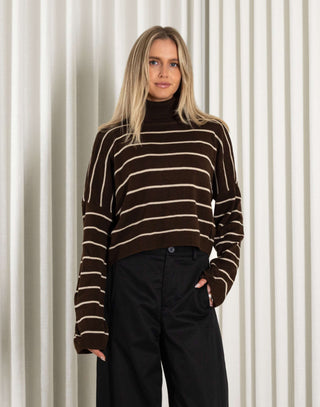woman wearing a brown and beige striped sweater against a white curtain background