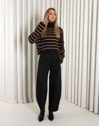woman wearing a brown and beige striped sweater against a white curtain background