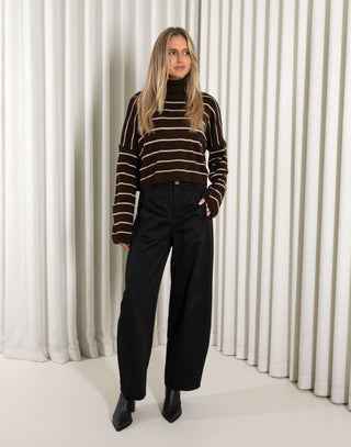 woman wearing a brown and beige striped sweater against a white curtain background