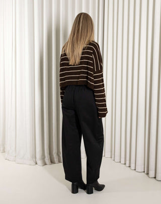 woman wearing a brown and beige striped sweater against a white curtain background