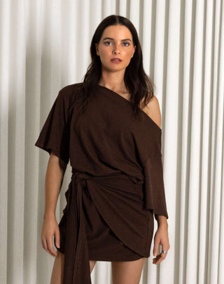 Woman wearing a brown dress with a draped design against a white curtain background Brown off shoulder mini dress with front drape detail