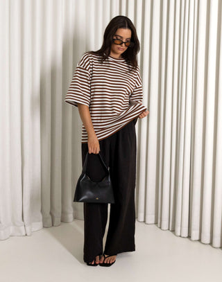 woman wearing a striped shirt and black pants standing against a white curtain background