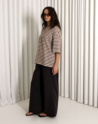 woman wearing a striped shirt and black pants standing against a white curtain background
