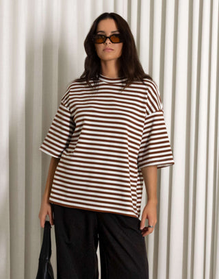 woman wearing a striped shirt and black pants standing against a white curtain background