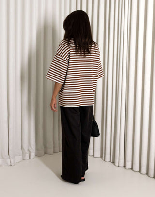 woman wearing a striped shirt and black pants standing against a white curtain background
