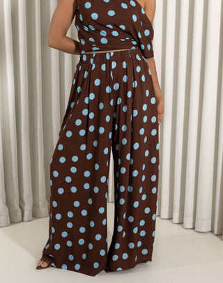 Brown jumpsuit with blue polka dots worn by a person against a neutral background Brown wide leg polka dot pants with relaxed fit