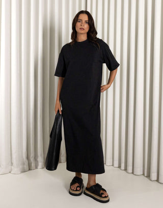 Woman wearing a black dress standing against a white curtain background Black relaxed fit midi dress with side leg split