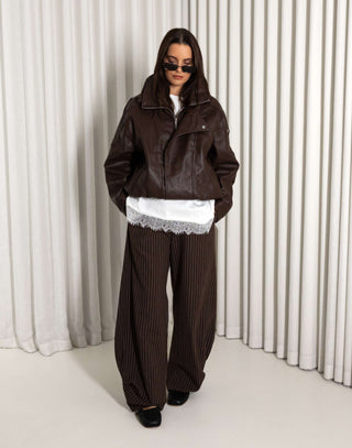 Person wearing a brown outfit with a white lace top againsat a white curtain background