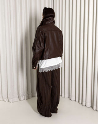 Person wearing a brown outfit with a white lace top againsat a white curtain background