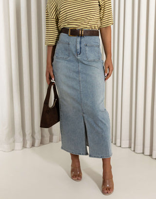 Person wearing a yellow striped shirt, blue denim skirt, and brown shoes against a white curtain background. Jonathan denim maxi skirt with front patch pockets and full stretch