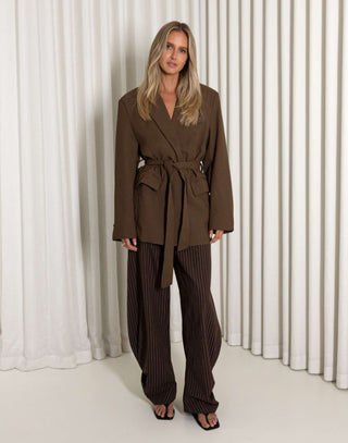Woman wearing a brown suit standing against a white curtain background