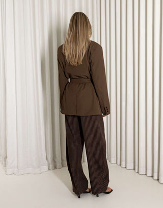 Woman wearing a brown suit standing against a white curtain background
