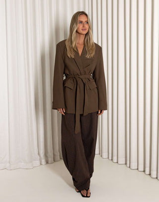 Woman wearing a brown suit standing against a white curtain background
