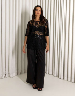 Woman wearing a black lace top and wide-leg pants against a white curtain background High waisted black straight leg pants