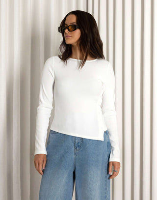 Person wearing a long sleeve white top with button side detail and blue wide leg jeans against a white curtain background