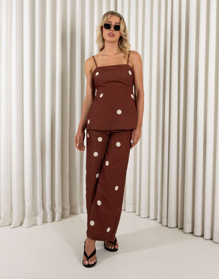 Woman wearing a brown polka dot outfit against a white curtain background Leo brown polka dot tie-back top and wide-leg pants set