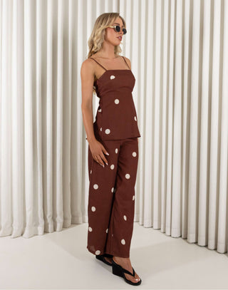 Woman wearing a brown polka dot outfit against a white curtain background Leo brown polka dot tie-back top and wide-leg pants set