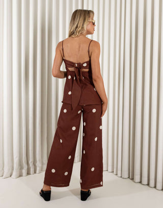 Woman wearing a brown polka dot outfit against a white curtain background Leo brown polka dot tie-back top and wide-leg pants set