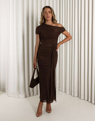 Woman wearing a brown off-shoulder dress with a belt, holding a brown handbag against a white curtain background. Lila brown off shoulder dress with side mesh loop tie